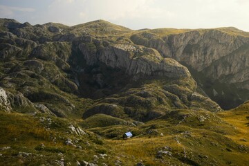 Aerial view of a small house under a rocky mountain landscape on a sunny day