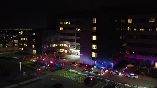 Fire Trucks And Police Cars Flashing Lights At Night In Front Of A Building In The City. - aerial