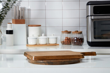 Stacked of wooden cutting board form an empty podium for display product. In the background is the counter with spice boxes, knife tray and microwave decorated on white tile background - Powered by Adobe