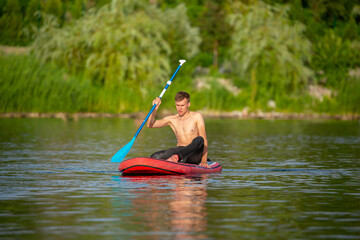 The guy swims on the SUP with an oar. Supsurfing on the lake. Board swimming.