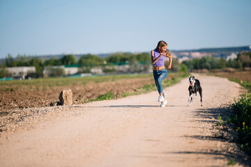 Fototapeta na wymiar Beautiful young blonde woman running in the field with her greyhound dog.