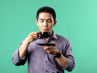 A portrait of an Asian man wearing a purple shirt, drinking coffee. Isolated on a green background.