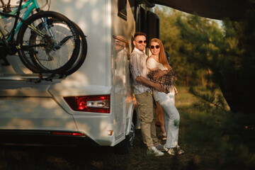 Obraz na płótnie Canvas A married couple with glasses stands next to their motorhome at sunset in the forest
