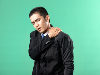 Fototapeta premium A portrait of an Asian man wearing a purple shirt, appearing to have lower back pain. Isolated on a green background.