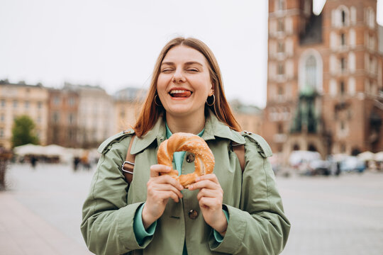 Attractive young female tourist is holding prezel, traditional polish snack on the Market square in Krakow. Traveling Europe in spring. High quality photo