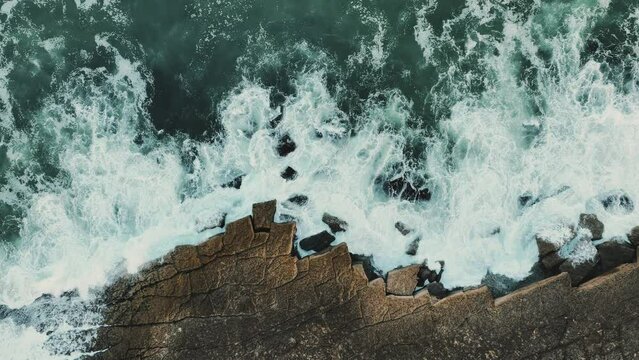 Aerial. White waves of the Atlantic Ocean crashing against a rocky shore