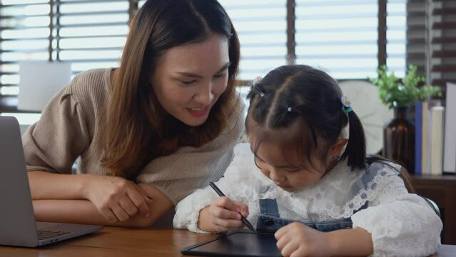 Asian young mother working with laptop computer at home and help daughter doing homework, Single mom freelancer work from home and helping his girl kid teaching homework on desk