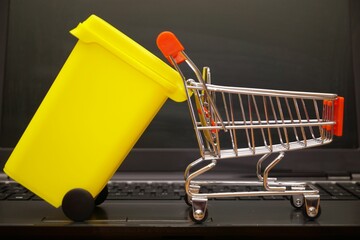 Miniature yellow bin an a shopping cart on a laptop representing electronic waste disposal