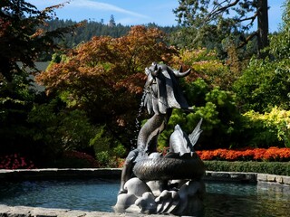 Sculpture of a serpent spitting water into a fountain in a lovely park surrounded by colorful trees