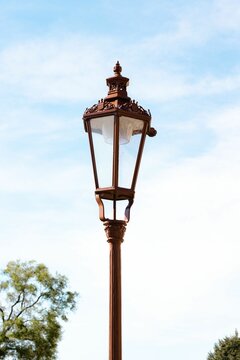 Vertical shot of a street lamp with a cloudy blue sky in the background