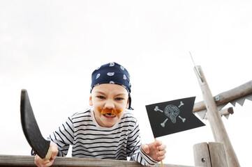 A little boy in pirate costume with a saber and a black pirate flag