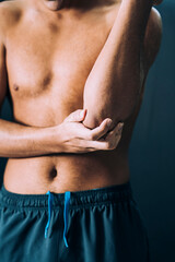 Fototapeta na wymiar Vertical closeup of a shirtless Caucasian male athlete rubbing his right elbow in pain