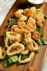 Vertical top closeup of fried calamari with tartar sauce on a wooden plate on the table