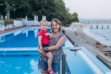 Fototapeta na wymiar Mom holds her daughter in arms by the seashore and the pool