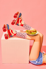 Slender female legs in vintage rollers with delicious hot-dog against pink background. Food and delivery service. Concept of pop art photography, creative vision, imagination. Minimal art