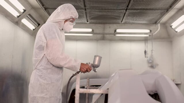 Car painting worker in white coat spray the lacquer to spare parts prepare to color it, safety worker working in painting room in the garage station, chronic sickness lacquer breathing to lung