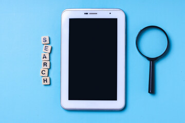 Magnifying glass, blank screen tablet smartphone and wooden cube lettering Search on blue background. Search Engine Optimization concept.