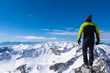 Wallpaper murals Himalayas A Tourist standing on a mountain top above the clouds and looking at the view. Direct sunlight. Clear blue sky. Winter. Mountaineering. High Tatras mountain in Poland and Slovakia