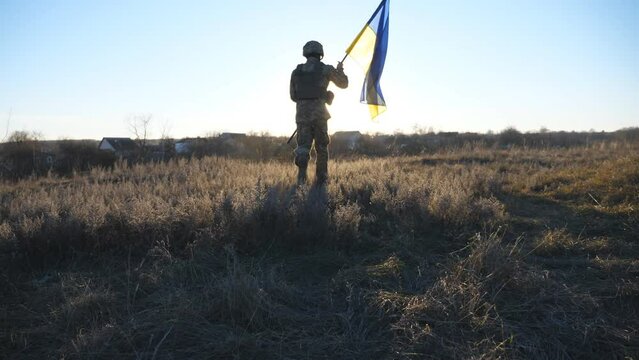 Male soldier of ukrainian army running with lifted national banner on the field. Young man in military uniform jogs with waving flag of Ukraine on the meadow. Concept of invasion resistance. Slow mo