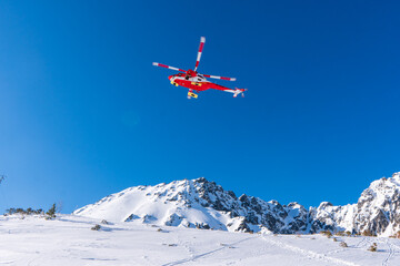 Naklejka na ściany i meble Red rescue helicopter moving in blue sky with blur propeller in winter mountains. Europe slovakia poland