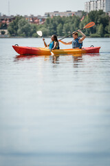 happy african american woman and young active man in life vests spending time on city lake and...