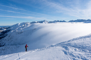 Adventurous women hiker on top of a steep rocky cliff overlooking winter alpine like moutain...
