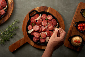 Portion of pepperoni sausage cut into slices. Served on a wooden board with a rustic iron plate.