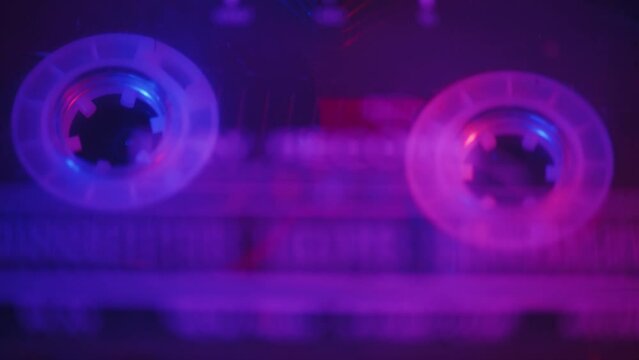 Audio engineer takes an audio cassette out of a professional tape recorder after the successful recording during the studio session in a color light in the view from above close up