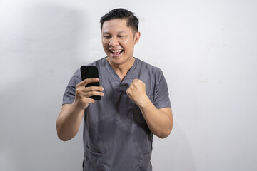 Excited Asian male medic laughing while looking at mobile phone