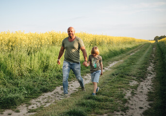 Naklejka na ściany i meble A man and a boy are walking and playing in a rapeseed field