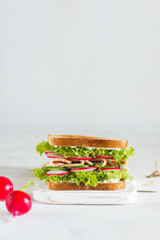 Delicious and fresh sandwich with greens, ham, cucumber and radish on a wooden board on a light background in the foreground with radish