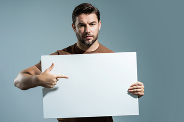Man with blank banner isolated on studio background. Portrait of attractive man with empty blank poster. Man showing poster, pointing finger on signboard placard. Male presenting billboard or banner.