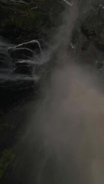 Vertical video. Extreme close dive tropical island waterfall speed water fall stream rainforest mountain valley aerial view. FPV sport drone drop shot jungle fern greenery woodland cliff creek pool 4k