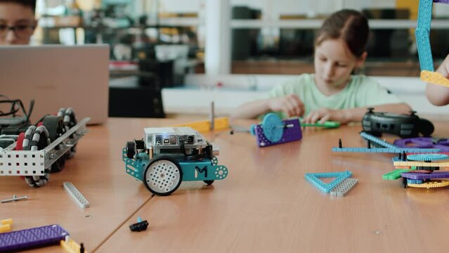 Schoolboy sitting at the table with other pupils in a class at a robotics lesson and controlling with a laptop an assembled robot which moving on the table. Concept of technological modern education