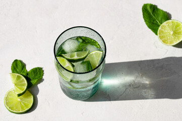 Summer refreshing cocktail Mojito with rum, mint, lime and ice in glass on a white stone background...