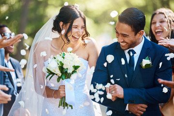 Love, wedding and couple walking with petals and guests throwing in celebration of romance. Happy, smile and young bride with bouquet and groom with crowd celebrating at the outdoor marriage ceremony - Powered by Adobe