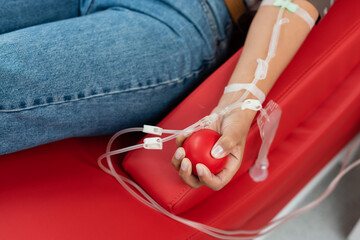 partial view of multiracial woman with a transfusion set holding rubber ball while sitting on...