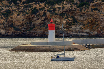 A sailing yacht enters the port of Cartagena. In the background is a red lighthouse. The waves...