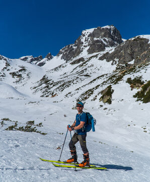 view of active man ski touring at mountains background at sunny winter day. Ski mountaineer with red jacket walking up along a steep snowy ridge with the skis in the backpack