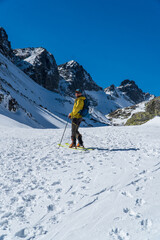 Fototapeta na wymiar view of active man ski touring at mountains background at sunny winter day. Ski mountaineer with red jacket walking up along a steep snowy ridge with the skis in the backpack