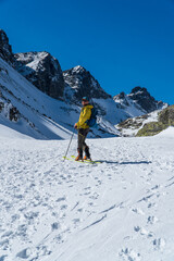 view of active man ski touring at mountains background at sunny winter day. Ski mountaineer with red jacket walking up along a steep snowy ridge with the skis in the backpack