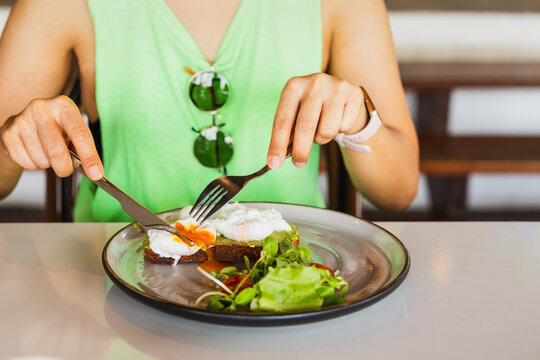 Woman eating breakfast of poached eggs on toast in restaurant.