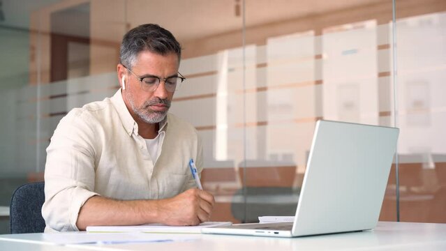 Middle-age Hispanic man using computer remote for business studying, watch online virtual webinar training meeting, video call. Smiling mature Indian or Latin businessman working on laptop in office.
