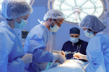 Four medical surgeons are in a room filled with different medical equipment working on a patient...