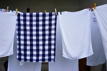 Weiße und blaue Handtücher hängen an Wäscheleine zum Trocknen bei Sonne am Morgen im Frühling