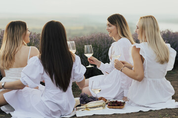 Group of friends having fun on picnic on the lavender field, sitting and drinking wine.