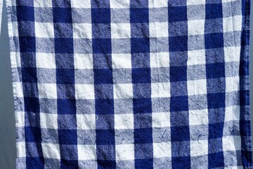Blau-weiß kariertes Geschirrhandtuch hängt auf Leine zum Trocknen bei Sonne am Mittag im Frühling