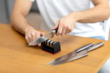 Fototapeta na wymiar Close-up photo of man sharpening knives with special knife sharpener at home