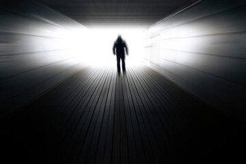 Obraz premium Blurred background with a silhouette of a man in a dark tunnel and light at the end