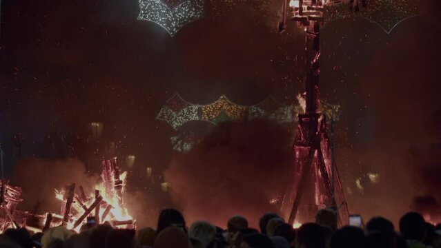 A crowd of people watches as an outdoor sculpture of a Ninot doll burns in a nocturnal festive bonfire Fallas, Valencia, Spain
